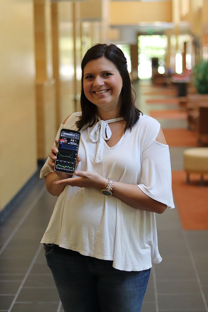 A woman in a white shirt is holding a cell phone in her hand.