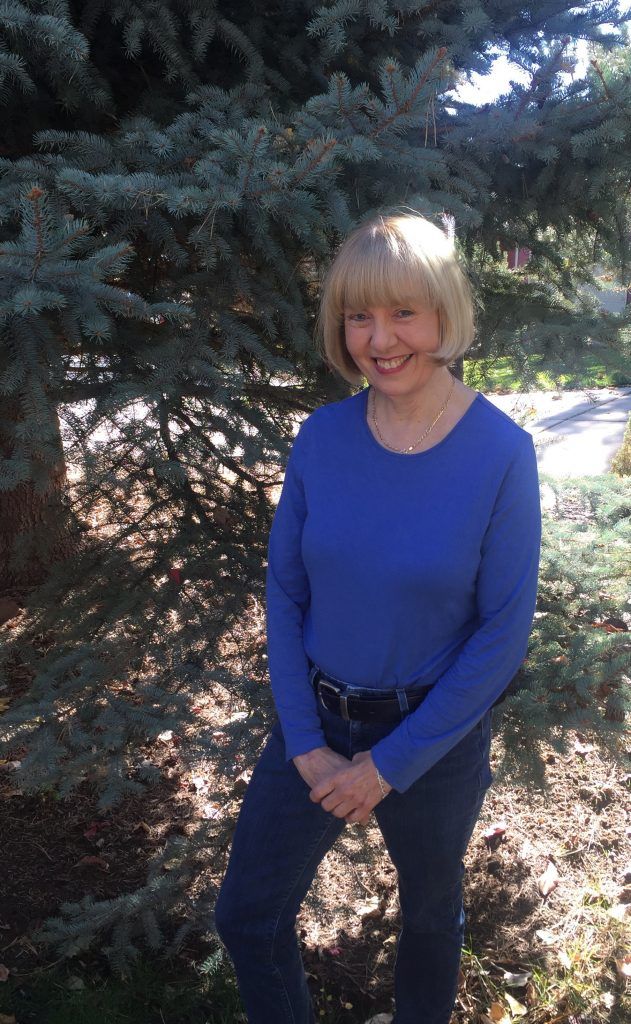 A woman in a blue shirt is standing in front of a tree.