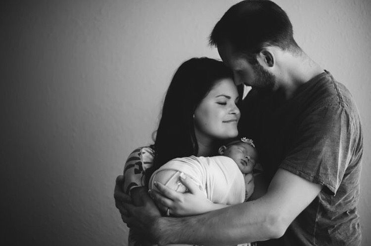 A black and white photo of a man and woman holding a newborn baby.