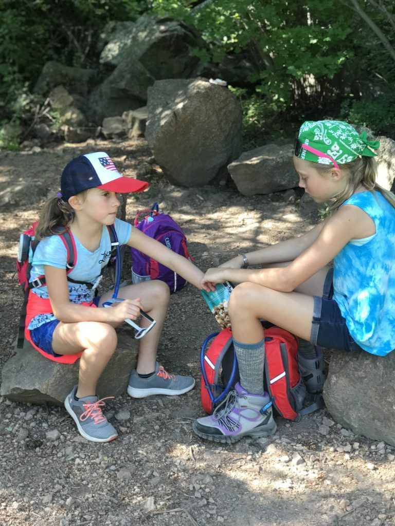Two young girls are sitting on a rock holding hands.