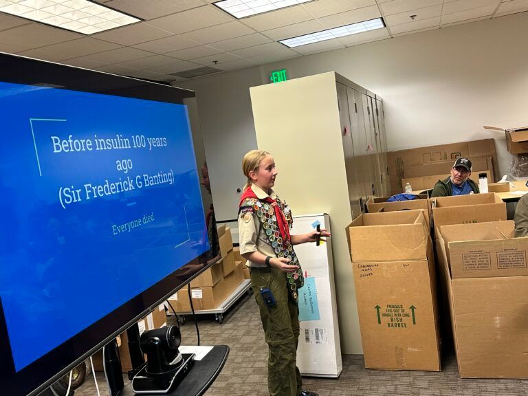 A boy scout is giving a presentation in front of a large screen.