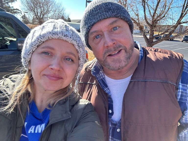 A man and a woman are posing for a picture in a parking lot.