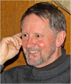 A man with a beard is smiling and touching his ear