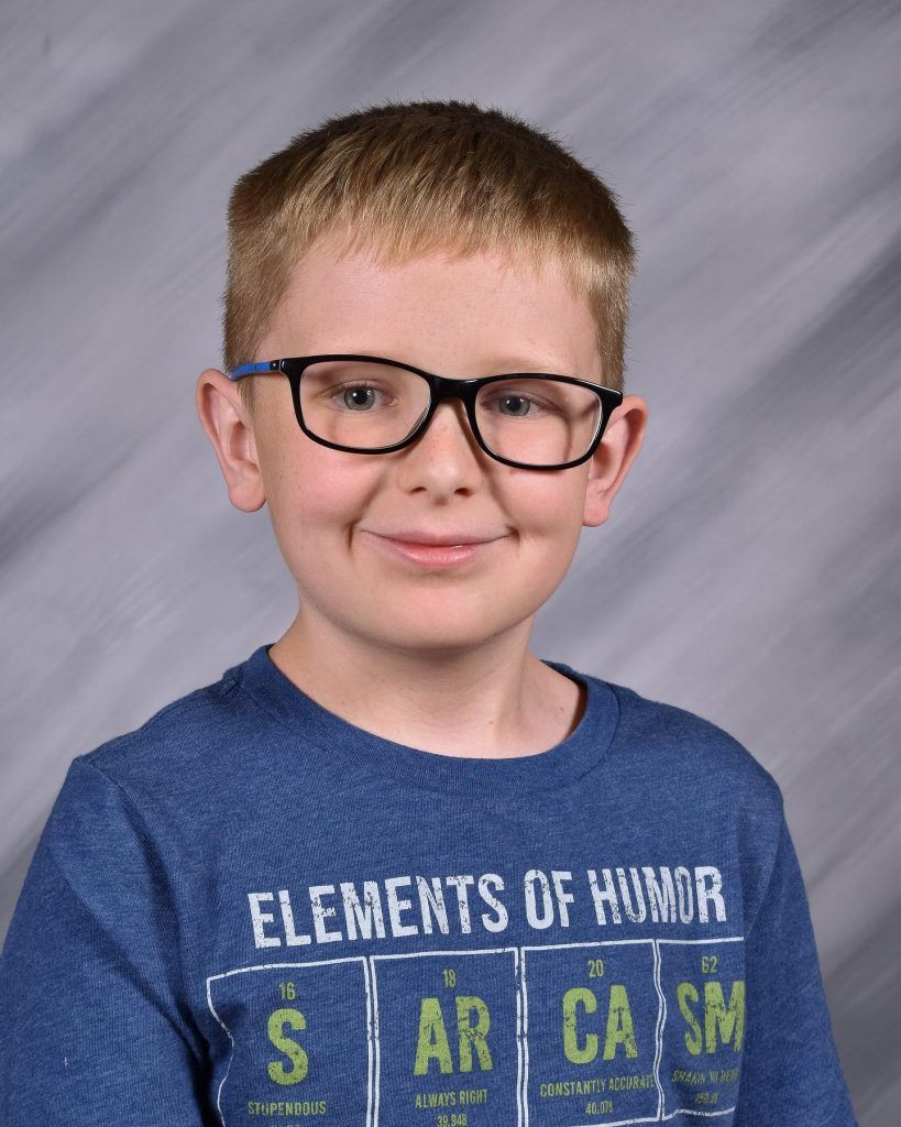 A young boy wearing glasses and a blue shirt that says elements of humor