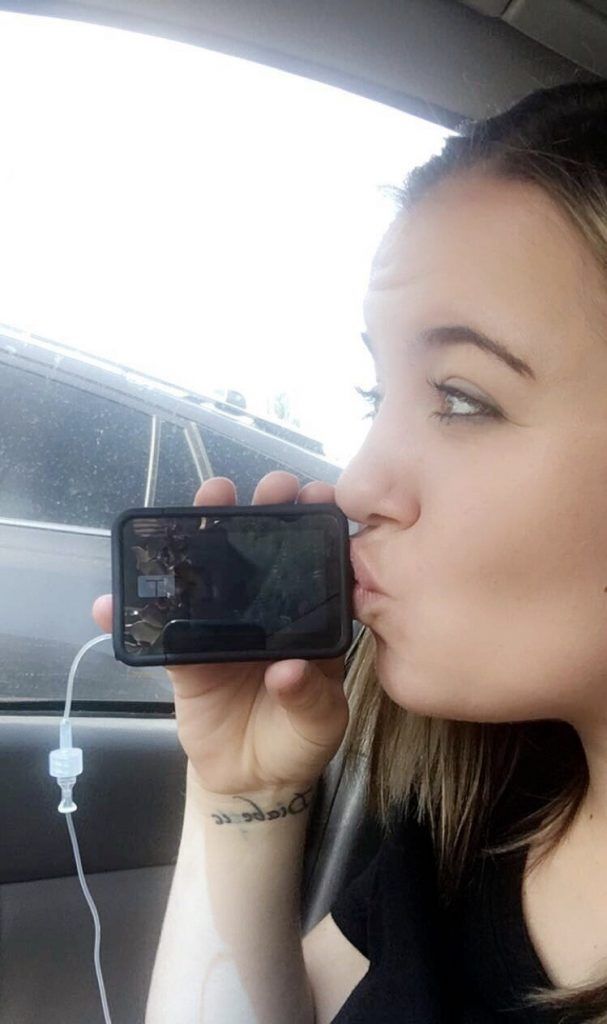 A woman is kissing a cell phone while sitting in a car.