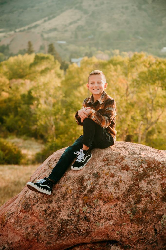 A young boy is sitting on top of a large rock.