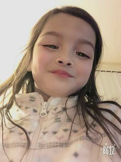 A little girl wearing a pink jacket is smiling for the camera.