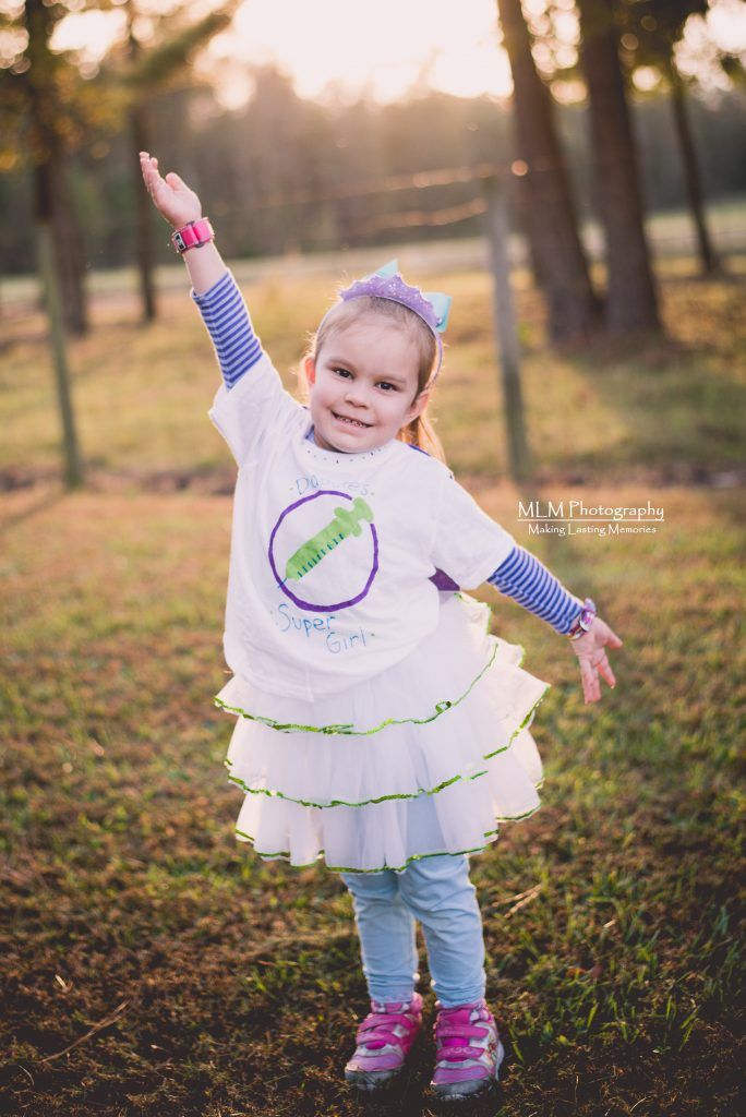 A little girl is standing in the grass with her arms outstretched.