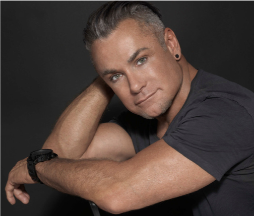 A man with a watch on his wrist looks at the camera