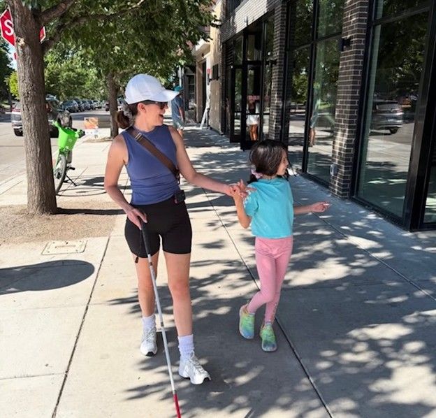 woman walking on sidewalk with her daughter and holding a blind cane