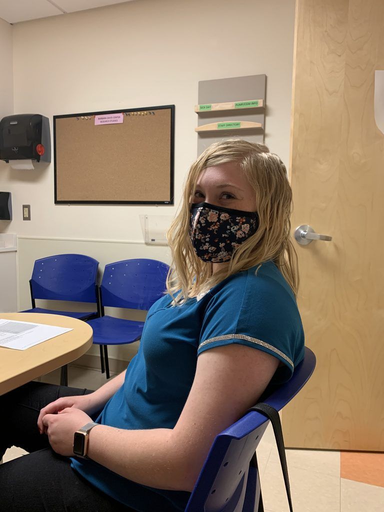 A woman wearing a mask is sitting in a chair in a room.