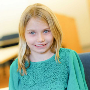 A young girl wearing a green lace top smiles for the camera