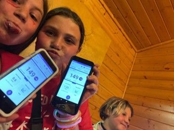 T1D camper Mia and her friend at camp with matching blood sugar levels on their phones