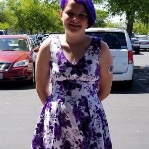 A girl with purple hair is wearing a purple and white floral dress.