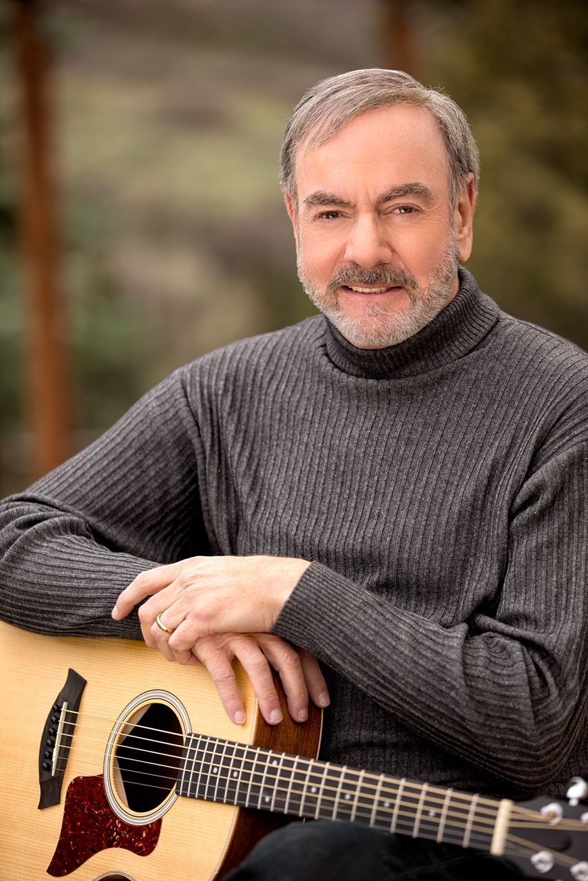 Neil Diamond smiling and holding his guitar.