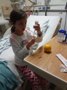 A little girl is sitting in a hospital bed holding a bottle.