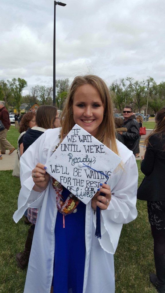 A woman in a white cap and gown is holding a graduation cap.
