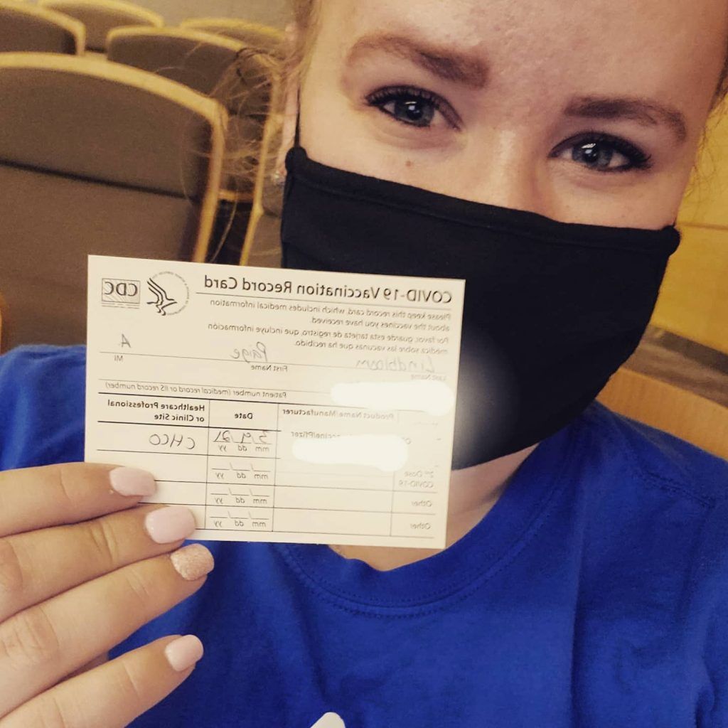 A woman wearing a mask is holding a vaccination card