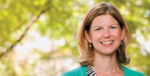 A woman in a green cardigan and striped shirt is smiling for the camera.