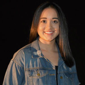 A young woman wearing a denim jacket is smiling for the camera.