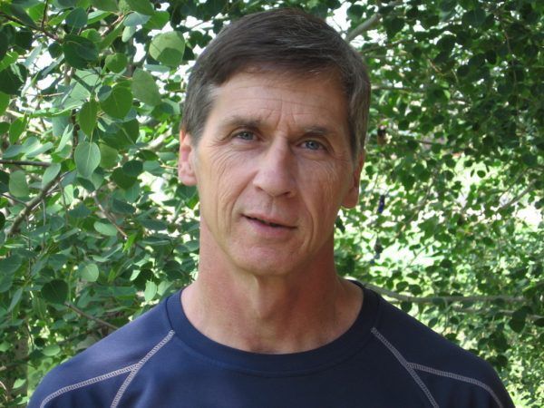 A man in a blue shirt is standing in front of trees