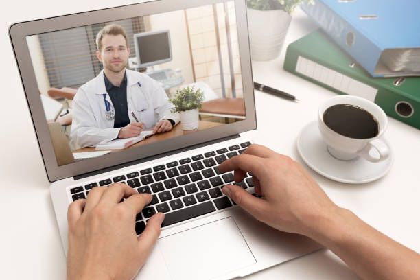 A person is typing on a laptop computer with a doctor on the screen.