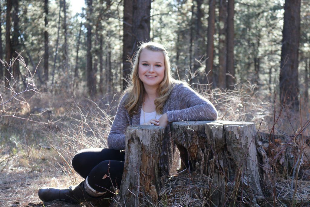 A woman is sitting on a tree stump in the woods.
