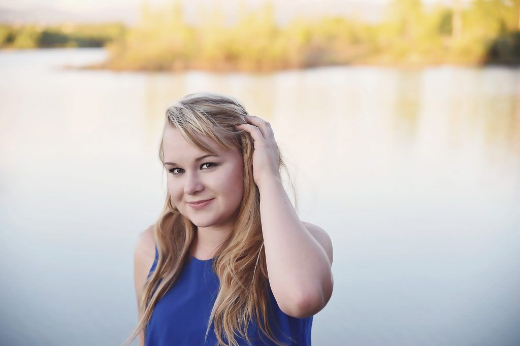 A woman in a blue dress is standing in front of a body of water.