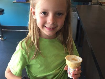 A little girl in a green shirt is holding an ice cream cone.