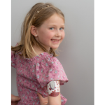 Young blonde girl with insulin pump on her arm in a pink shirt. 