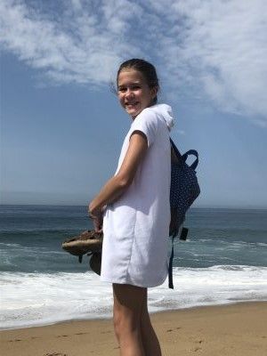 A young girl is standing on a beach holding a pair of flip flops.