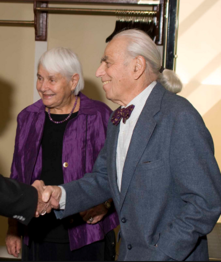 A man in a suit shakes hands with a woman in a purple jacket