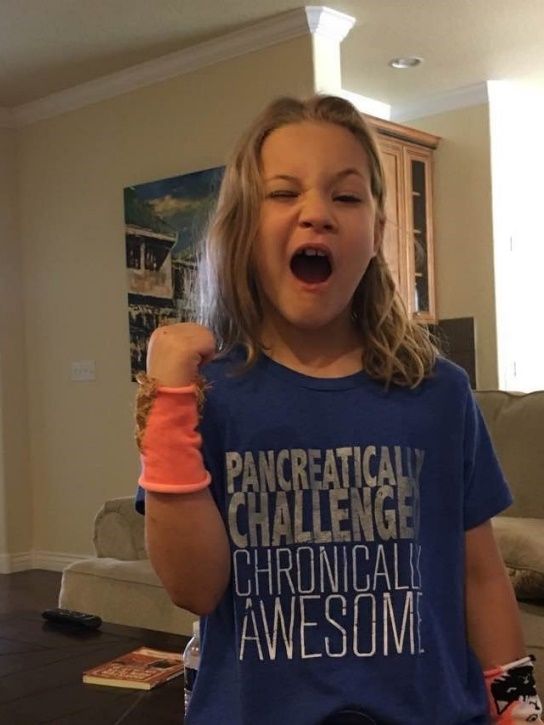 A young girl wearing a blue shirt that says pancreatic challenge chronically awesome