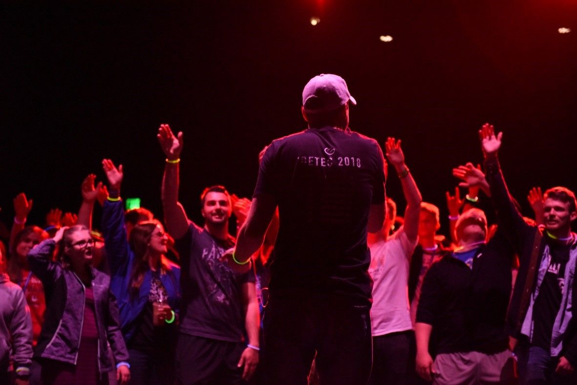 A man is standing in front of a crowd of people with their hands in the air.