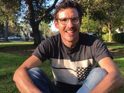 A man wearing glasses is sitting on the grass in a park