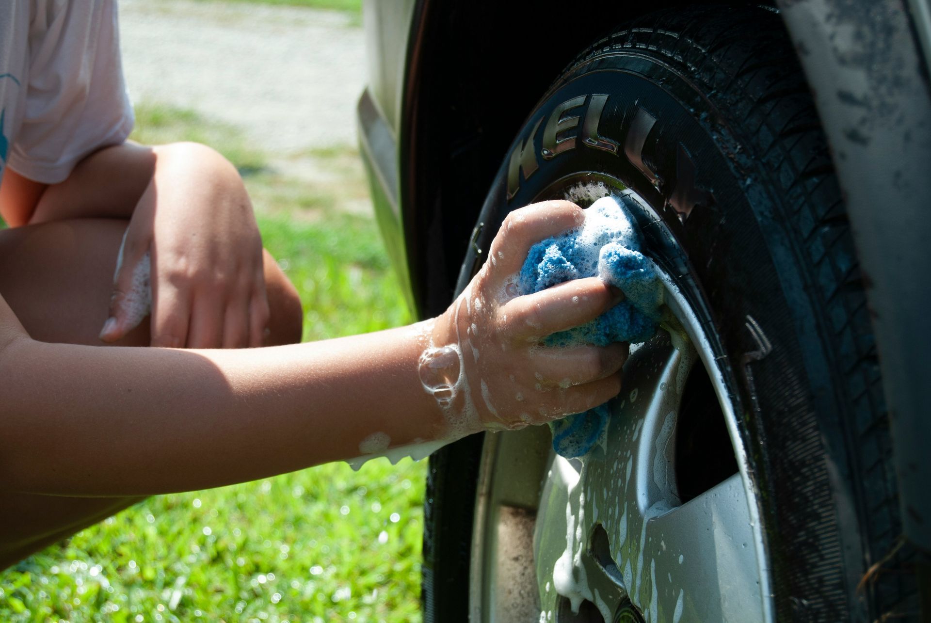 Closeup of teen washing the wheel of a car at car wash fundraiser.