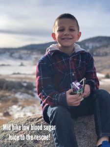 A young boy is sitting on a rock holding a box of juice.