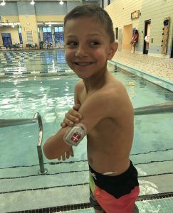 Gavin standing by the pool showing his insulin pump on his arm