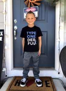 A young boy wearing a type one der ful t-shirt is standing in front of a door.