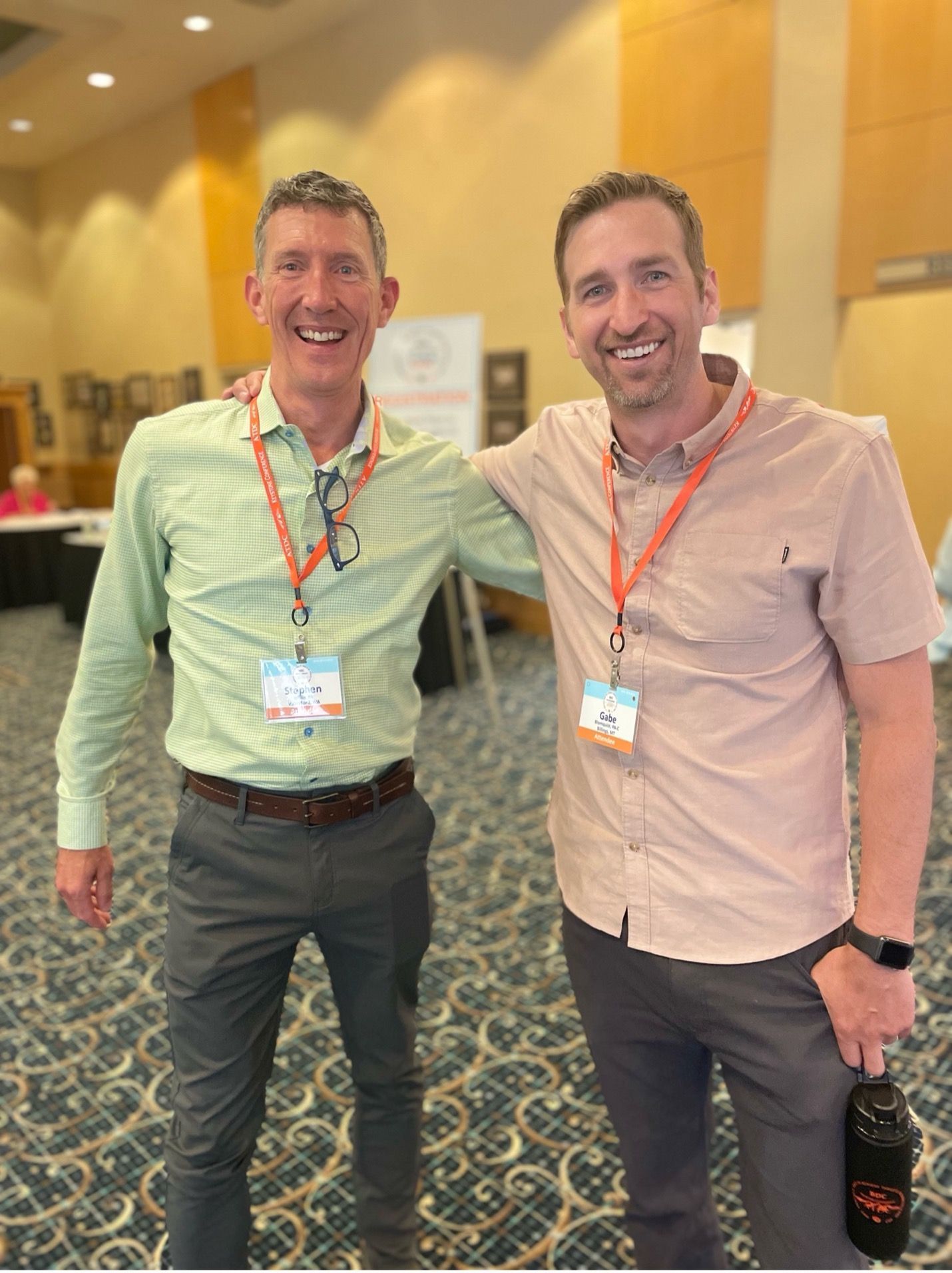 Two smiling male ATDC attendees with conference lanyards around their necks.