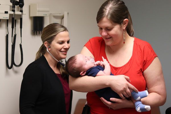 A woman is holding a baby while another woman listens to it with a stethoscope