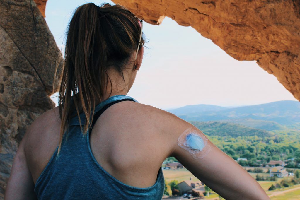 A woman with a patch on her arm is looking out of a cave.