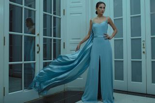 A woman in a long blue dress is standing in front of a door.