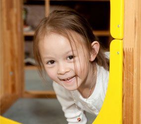 A little girl is looking through a yellow fence.