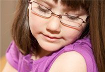 A little girl wearing glasses and a purple shirt is looking down.