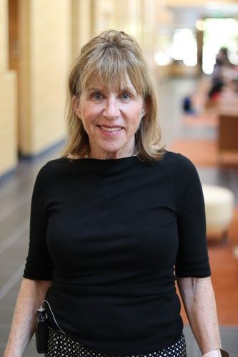 A woman is standing in a hallway wearing a black shirt and smiling.