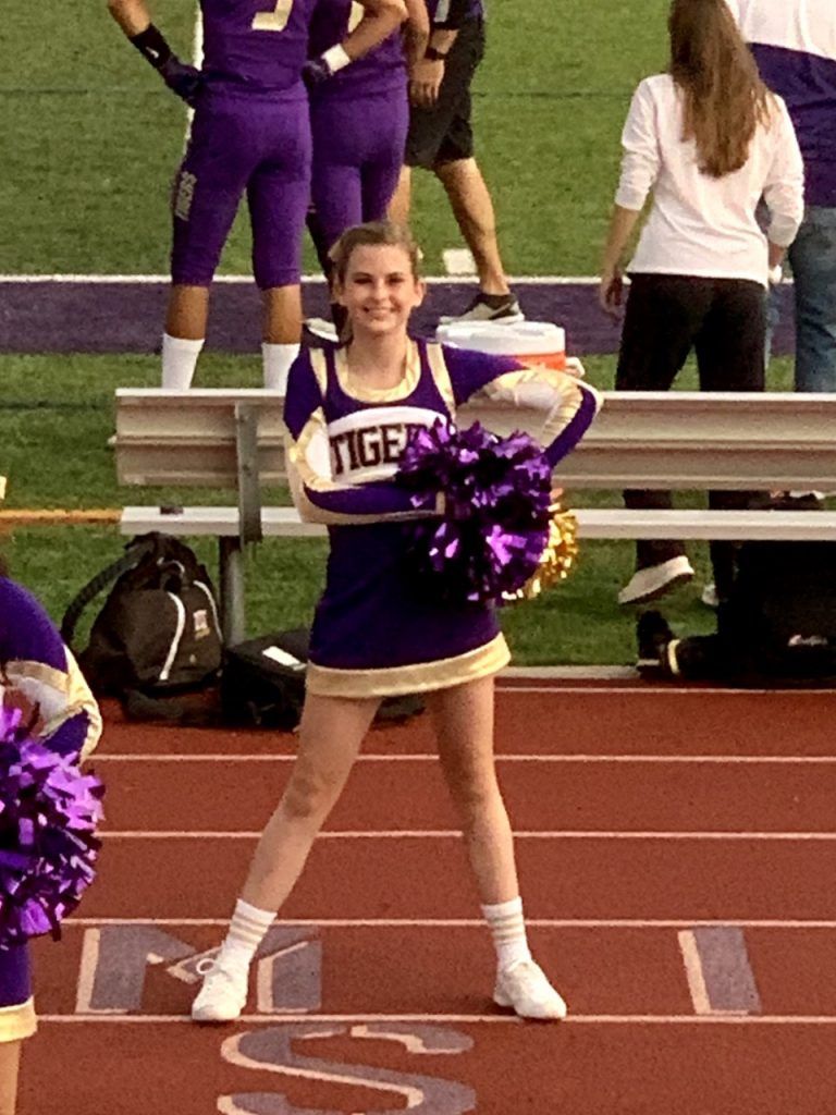 A cheerleader for the tigers is holding pom poms