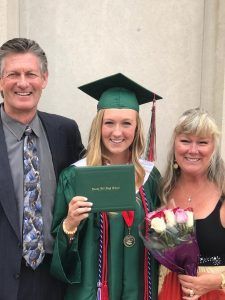 A woman in a graduation cap and gown is posing for a picture with her parents.