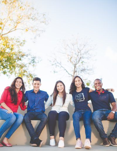 Group of five young smiling adults posing together on a bench.