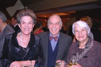 A man and two women are posing for a picture and the man is wearing a bow tie.